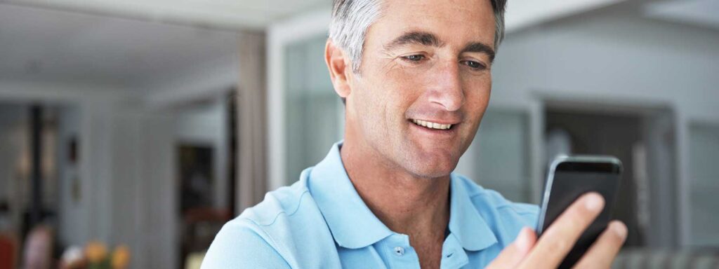 An older man smiling while looking at his phone